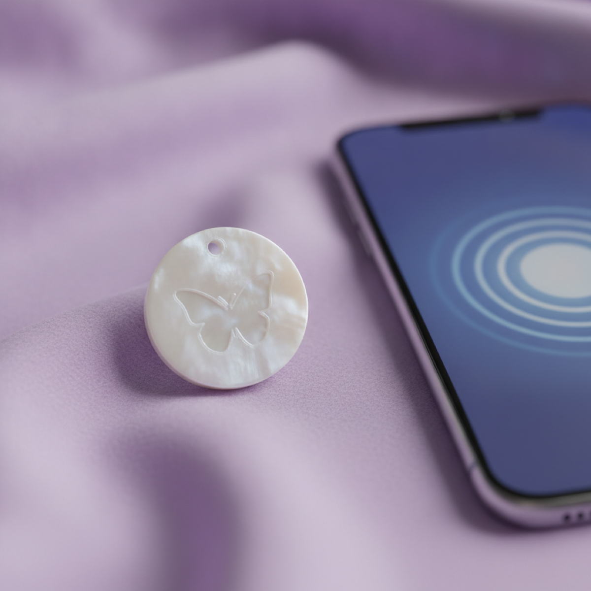 A small round 3D-printed tag with a butterfly on it, resting beside a phone